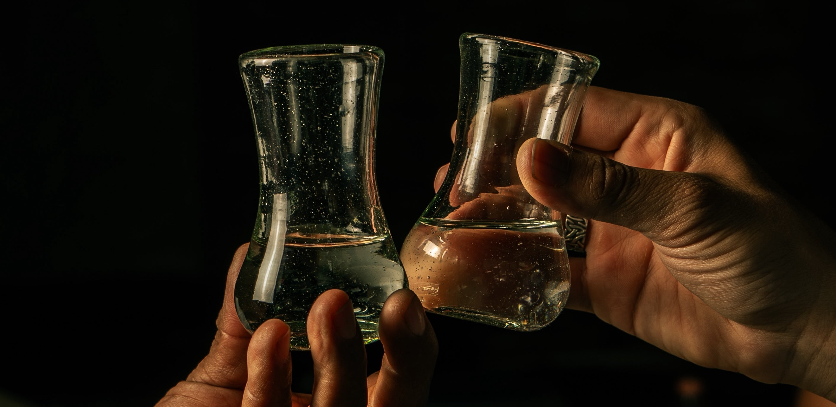 Two people clinking mezcal glasses